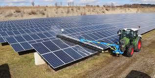 Traktor, der Solarpanels säubert; großes Solarfeld, hellblauer Himmel, interessantes Gerät.