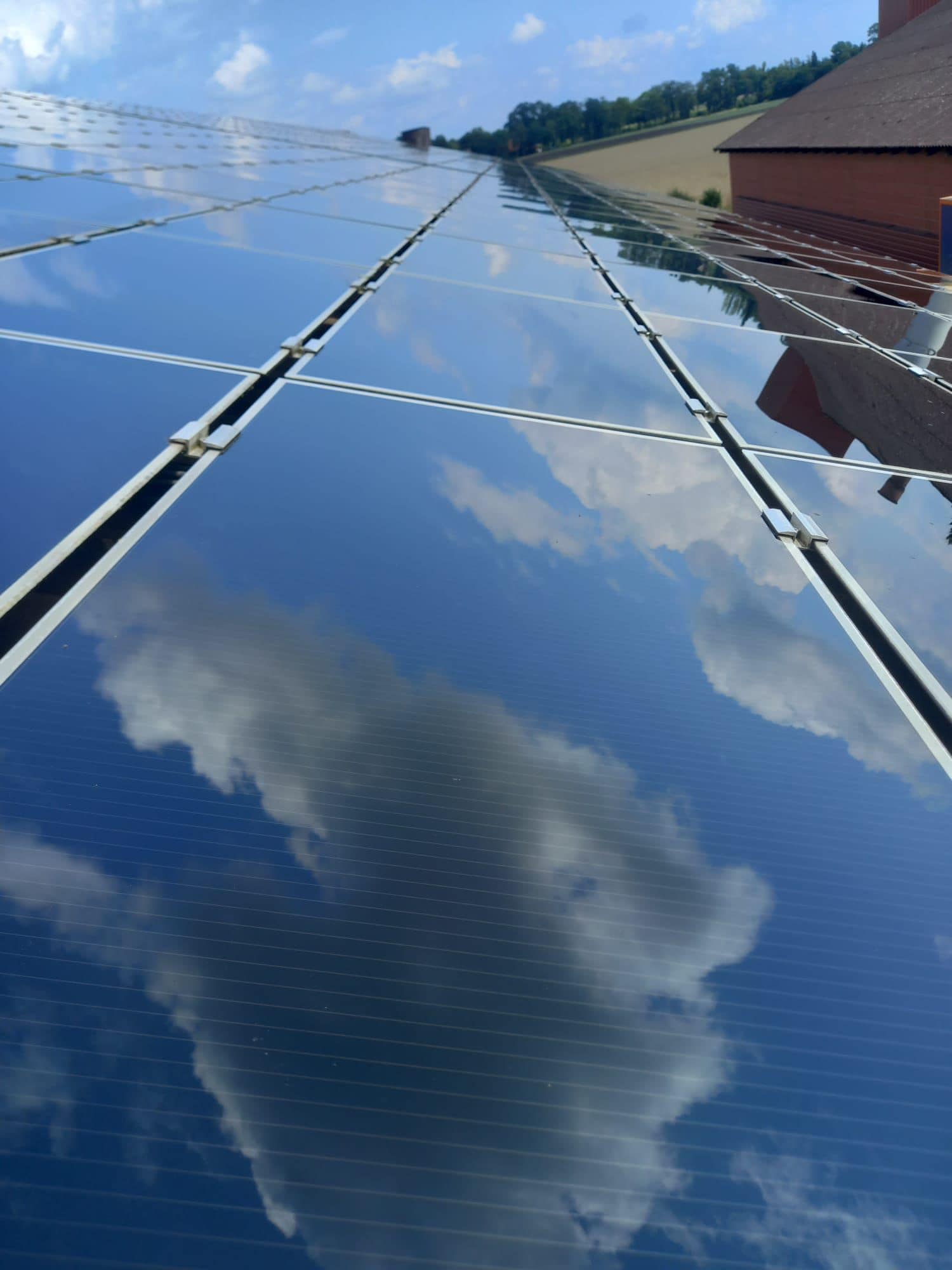 Spiegelung von Wolken auf blauen Solarpaneelen, in ländlicher Umgebung mit grünem Hügel.