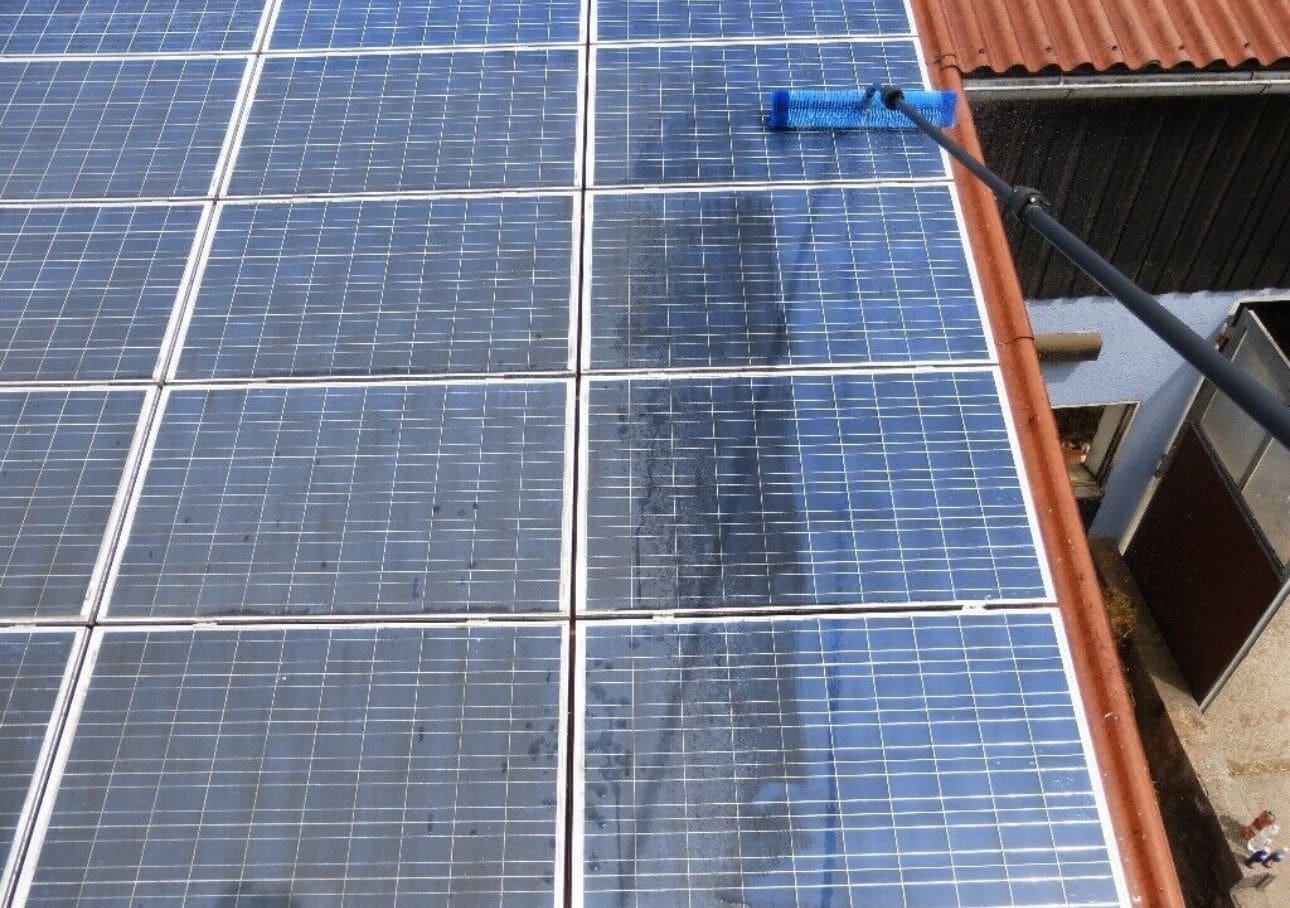 Solarpanels werden mit einer blauen Bürste gereinigt; teils sauber, teils noch schmutzig.