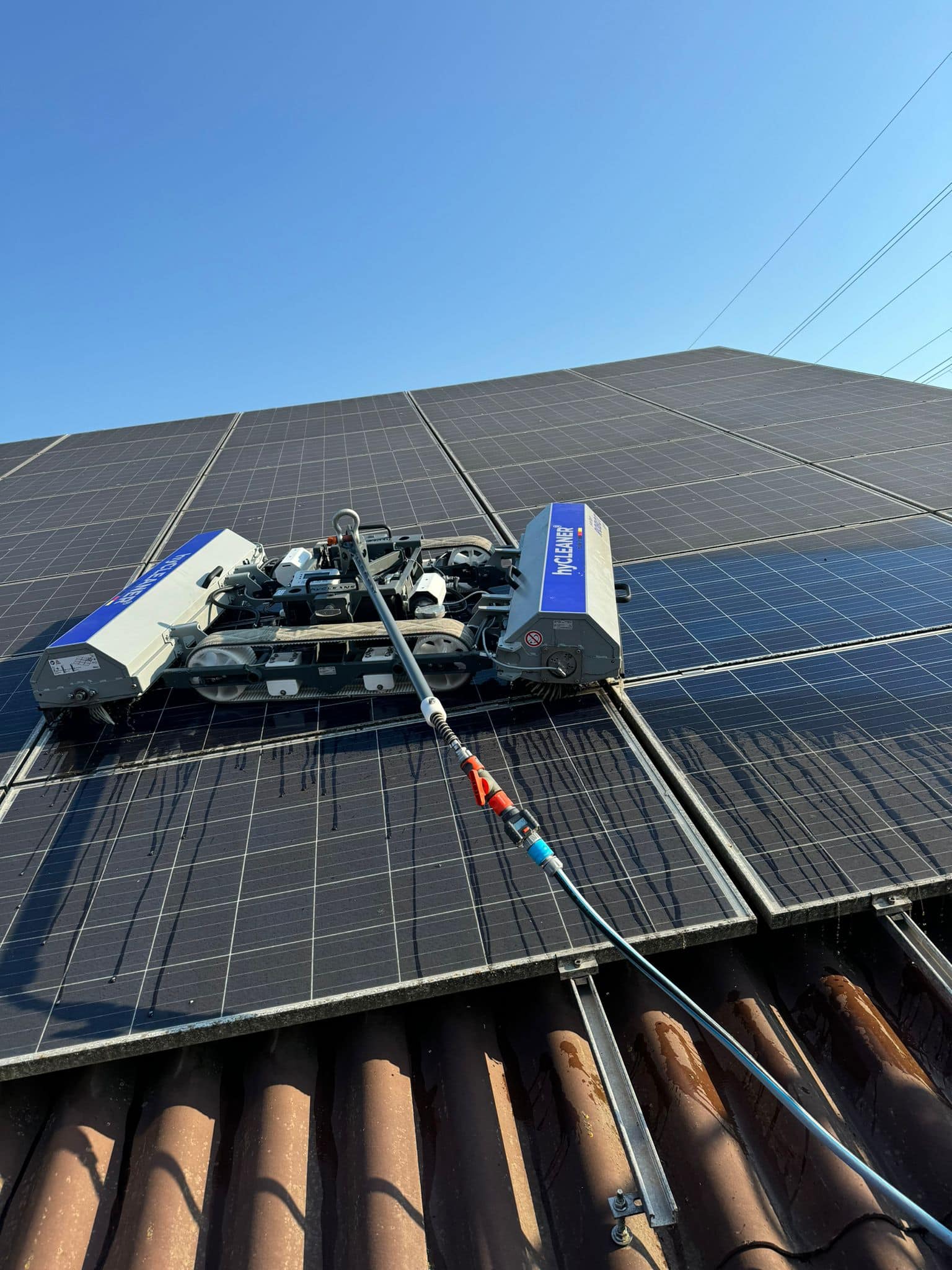 Ein Reinigungsroboter auf schwarzen Solarpaneelen bei blauem Himmel in Aktion.