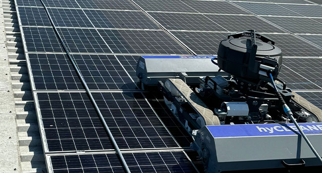 Solarpanel-Reinigungsroboter auf Dach, metallisch, blaue Akzente, bei der Arbeit, Sonnenlicht reflektierend.